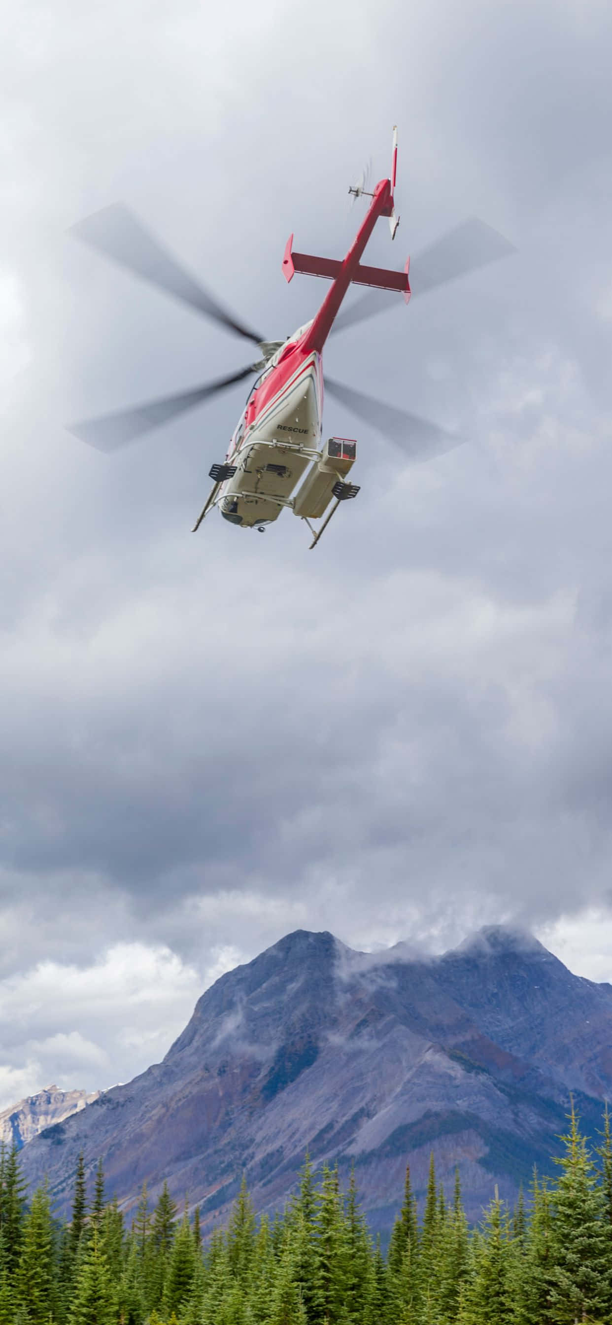 en helikopter flyvende over en skov med bjerge i baggrunden Wallpapers
