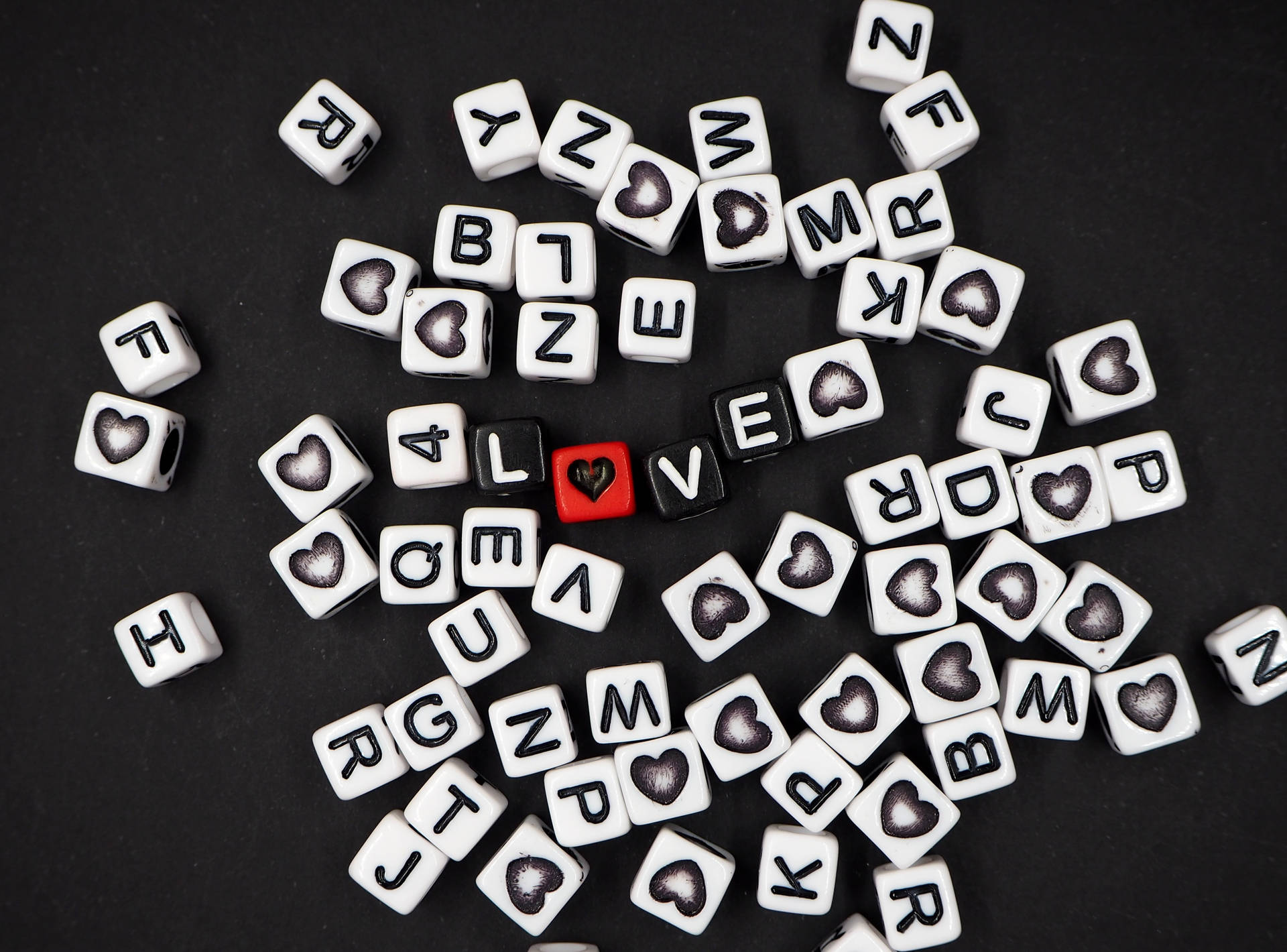 Sorte terninger, der danner ordet "love" med et hjerte, der erstatter "O", og spredte bogstaver af hvide terninger på en sort overflade til Hjertensdag. — Kærlighed Wallpapers
