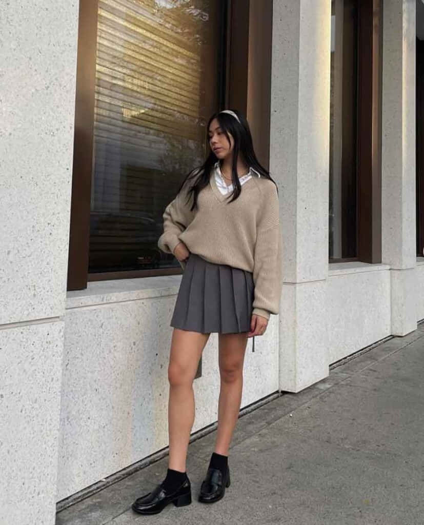 Kvinde i sweater og nederdel stående ved en væg Wallpapers