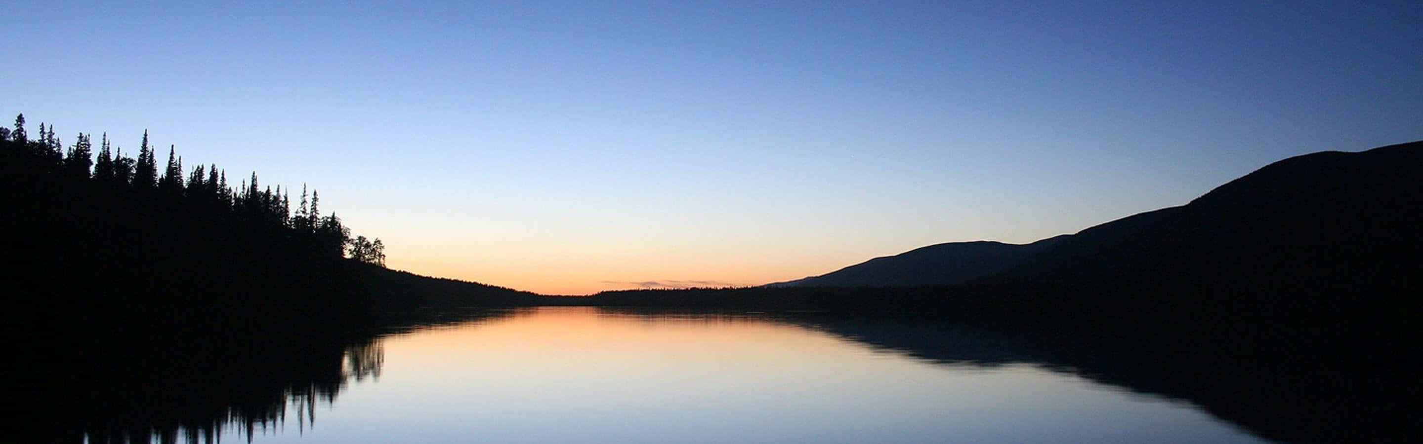 Rolig sø ved solnedgang på flere skærme Wallpapers