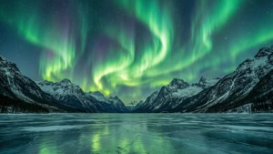 En smuk grøn nordlys oplyser nattehimlen over sneklædte bjerge. wallpaper