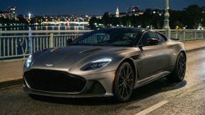 Aston Martin DBS Superleggera på en bro om natten med byens lys. wallpaper