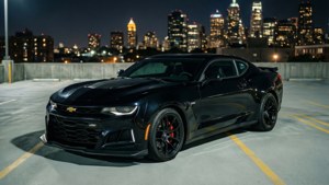 En sort Camaro ZL1 holder på en tagparkering med byens skyline om natten. wallpaper