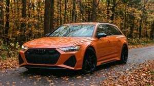 En orange Audi RS6 Avant på en efterårs skovvej med faldende blade.