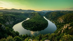 En bugtende flod spejler en grøn himmel gennem en frodig dal med fjerne bjerge. — Grøn himmel Wallpapers