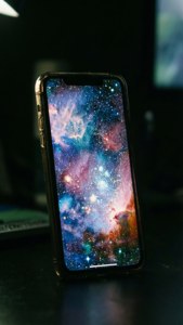 iPhone 17-skærm, der lyser med galaksebaggrund i mørke.