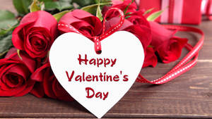Buket af røde roser liggende på bordet med et hvidt hjertekort, hvor der står "Glædelig Valentinsdag". — Chromebook Wallpapers