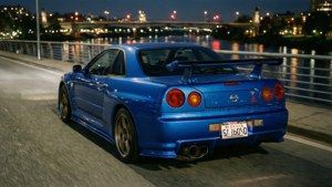 En blå Nissan GT-R på en bro om natten med byens spejlinger.