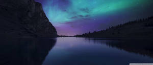 Ultrawide nordlys i farverige pastelblå og lilla himmel med stjerner set fra bjergene.