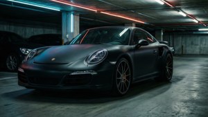 En mat sort Porsche 911 Turbo S skiller sig ud i en dyster undergrundsgarage med neonrefleksioner. wallpaper