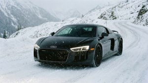 En sort Audi R8 kører ad en sneklædt alpevej med faldende sne.