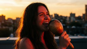 Vivo synger en følelsesladet sang på et tag, mens solen går ned, med en maraca i hånden.