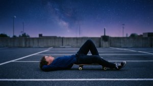 En skaterdreng, der slapper af under en stjernehimmel på en stille plads.