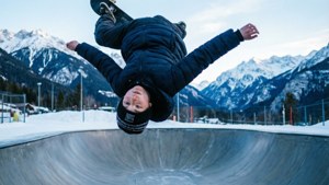 Skaterdreng udfører 360 flip på halfpipe i snedækket bjergmiljø.