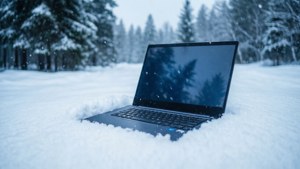 En Chromebook placeret i sne med en sneklædt skov som baggrund.